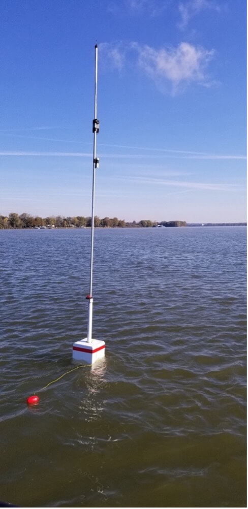Floating buoy with square base and long pole on top of it floats in the waterway