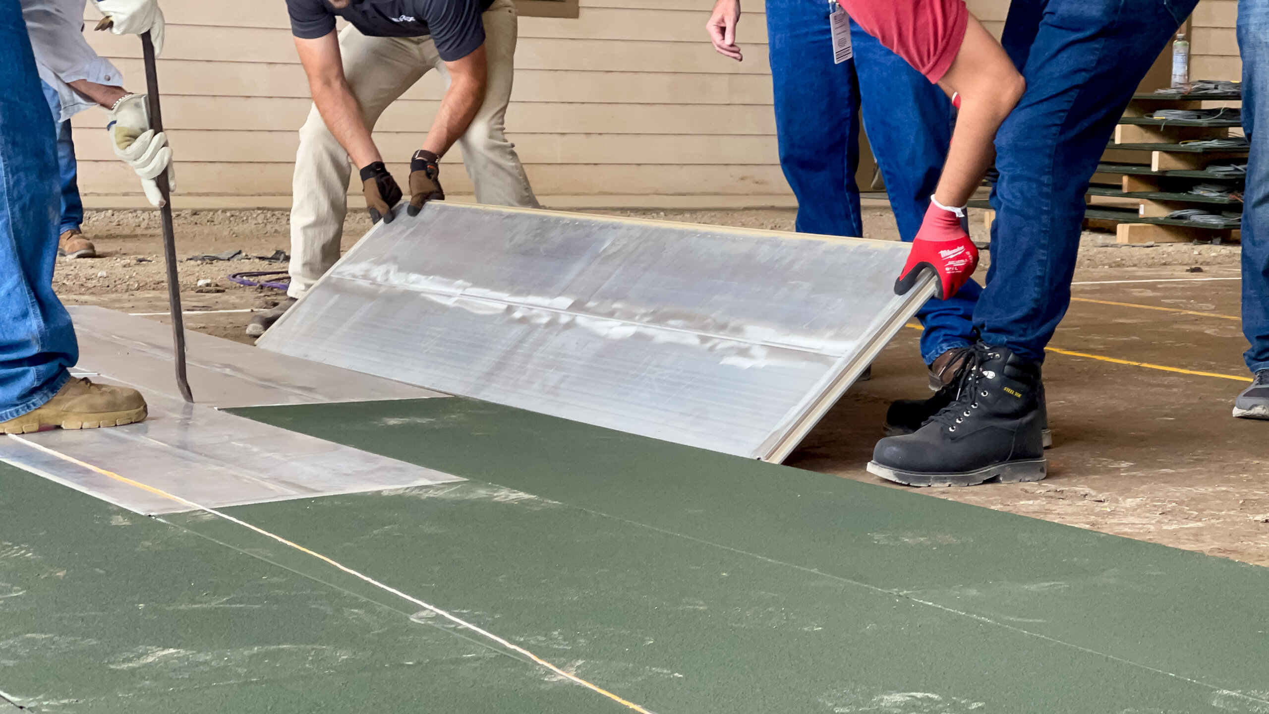 Workers with gloved hands lift and position a rectangular panel on a prepared soil surface.