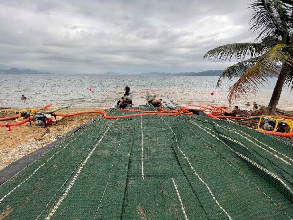 Workers and orange hoses on a green mat on a beach